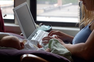 Baby watches on as mother types on laptop